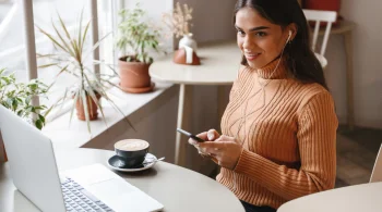 A woman smiles in a cafe while reviewing her business's social media account.