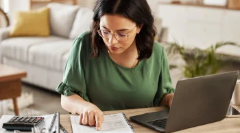 A woman reads a ledger from her business and enters the data into her laptop.